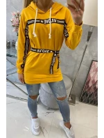 Šaty zdobené stuhou a nápisy v hořčicové barvě Šaty zdobené stuhou a nápisy v hořčicové barvě